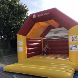 Auf dem Bild ist eine aufgebaute Hüpfburg mit drei Kindern darauf zu sehen.