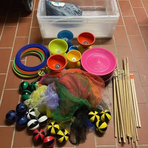 Auf dem Bild ist die Kiste des Sets sowie der Inhalt zu sehen. Es besteht aus 21 Jonglierringen, 7 Jongliertellern, 7 Jonglierstäben, 7 Diabolos, 7 Diabolostäben, 21 Jonglierbällen und 21 Jongliertüchern.