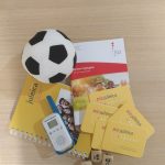 Auf dem Bild ist ein kleiner Stofffußball, ein Walkie Talkie, drei Würfel mit Gesichtern und Juleica und kja Unterlagen zu sehen